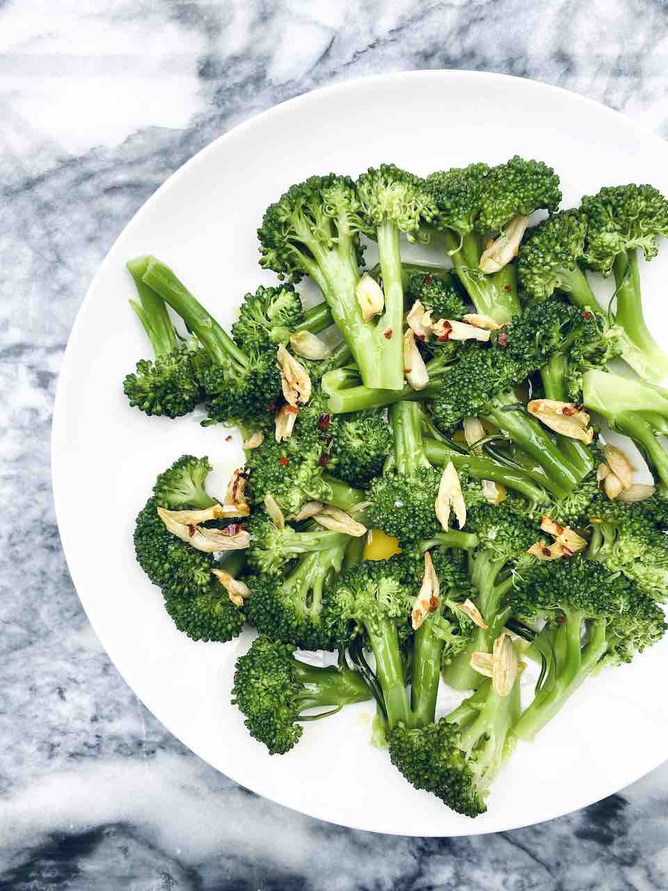 Cooked broccoli florets with garlic on a white plate